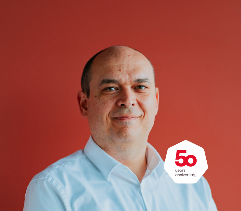 Portret van Cristian Musat, Managing Director EOS Technology Solutions, die voor een rode achtergrond staat.