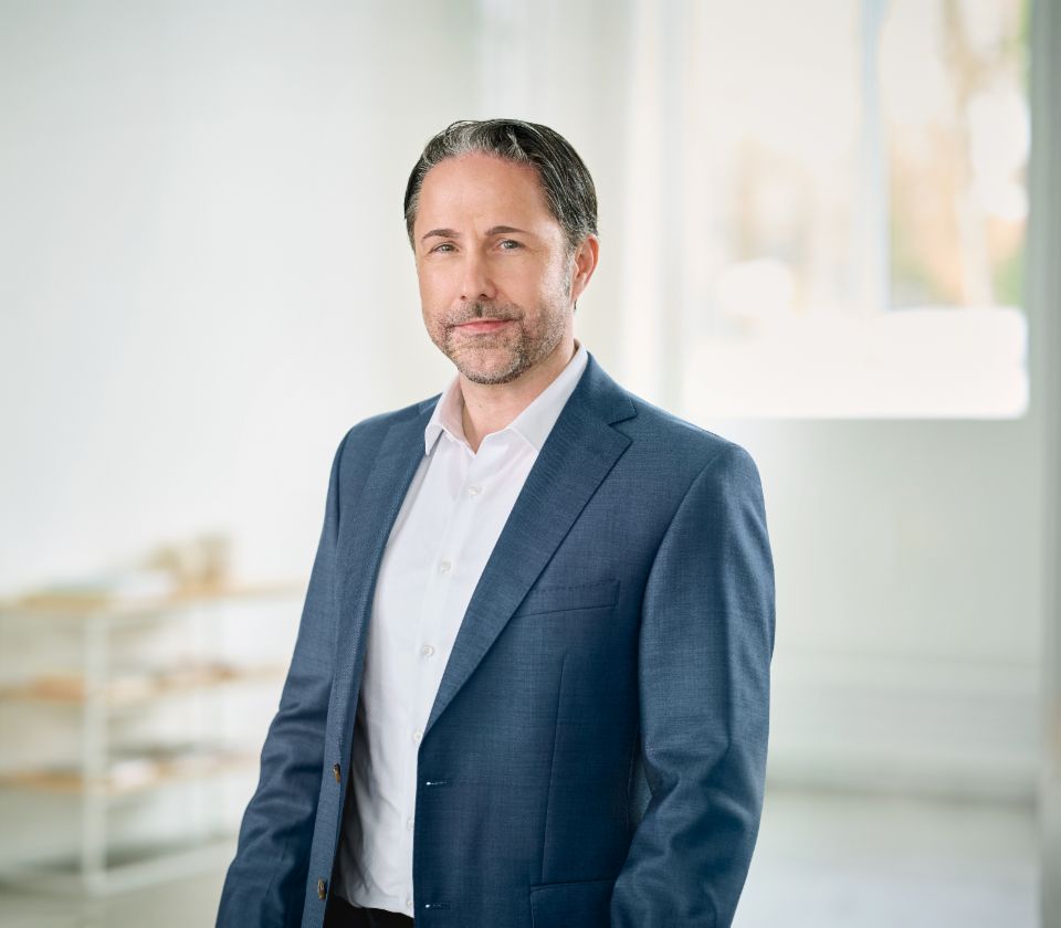 Portret van Marwin Ramcke, voorzitter van de Raad van Bestuur van de EOS-groep, die in een heldere ruimte zit en een donkere blazer draagt. 