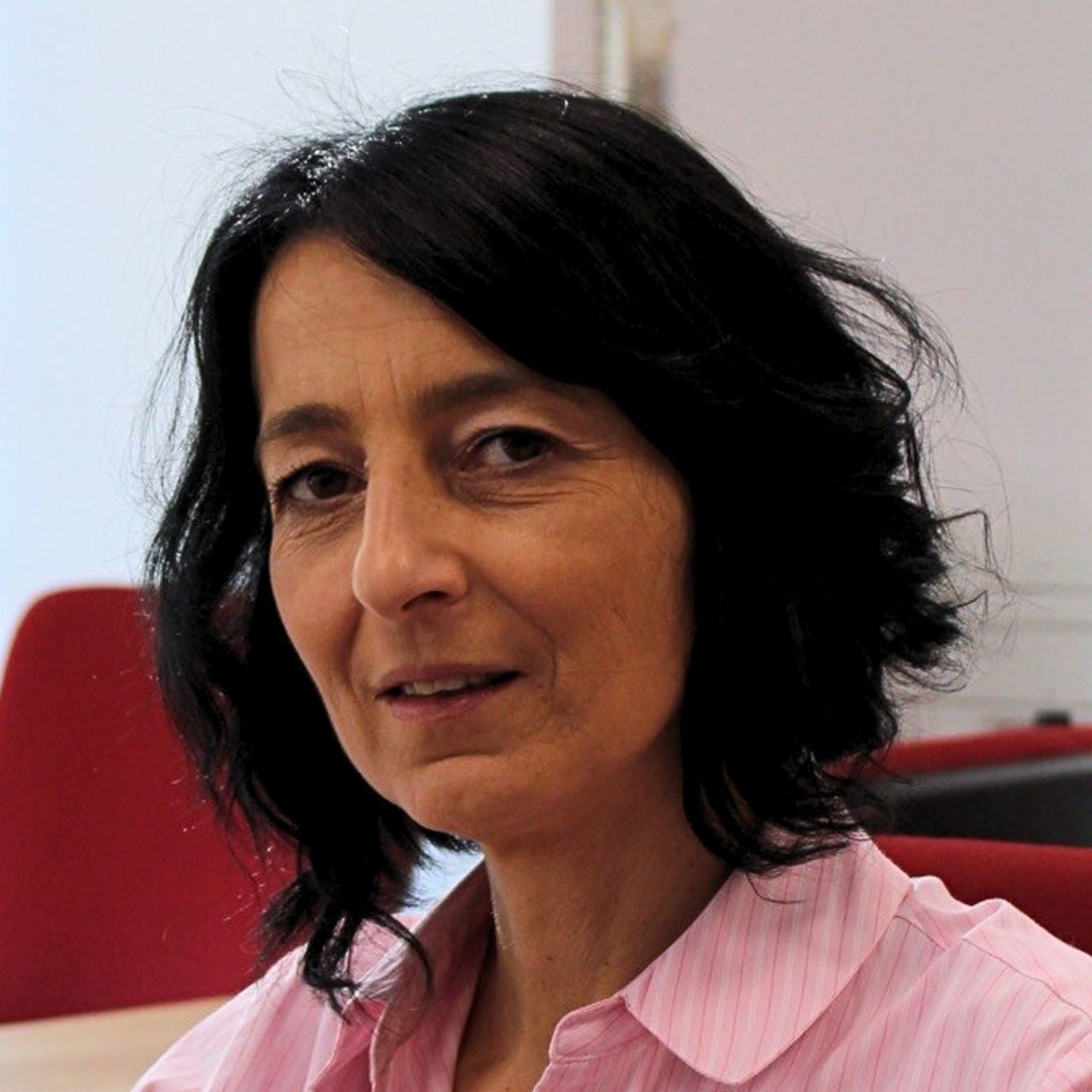Cristina Pasere, Responsable du Support Opérationnel de Conformité chez EOS Roumanie, est assise à son bureau, vêtue d'un chemisier rayé rose, et regarde la caméra.