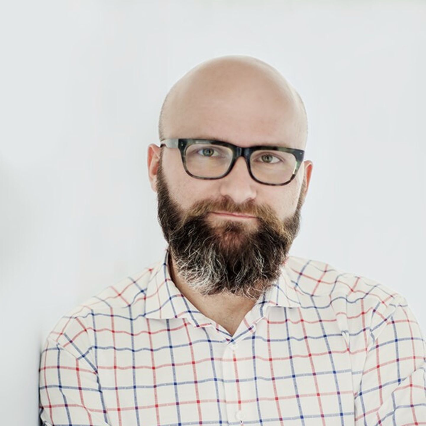 Dr. hab. Tomasz Piekot avec une chemise à carreaux s'appuyant contre un mur blanc.