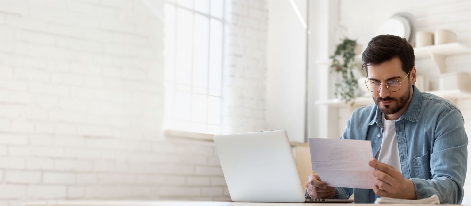 Man met bril werkt op laptop terwijl hij schuldregelingsdocument bekijkt in licht huis