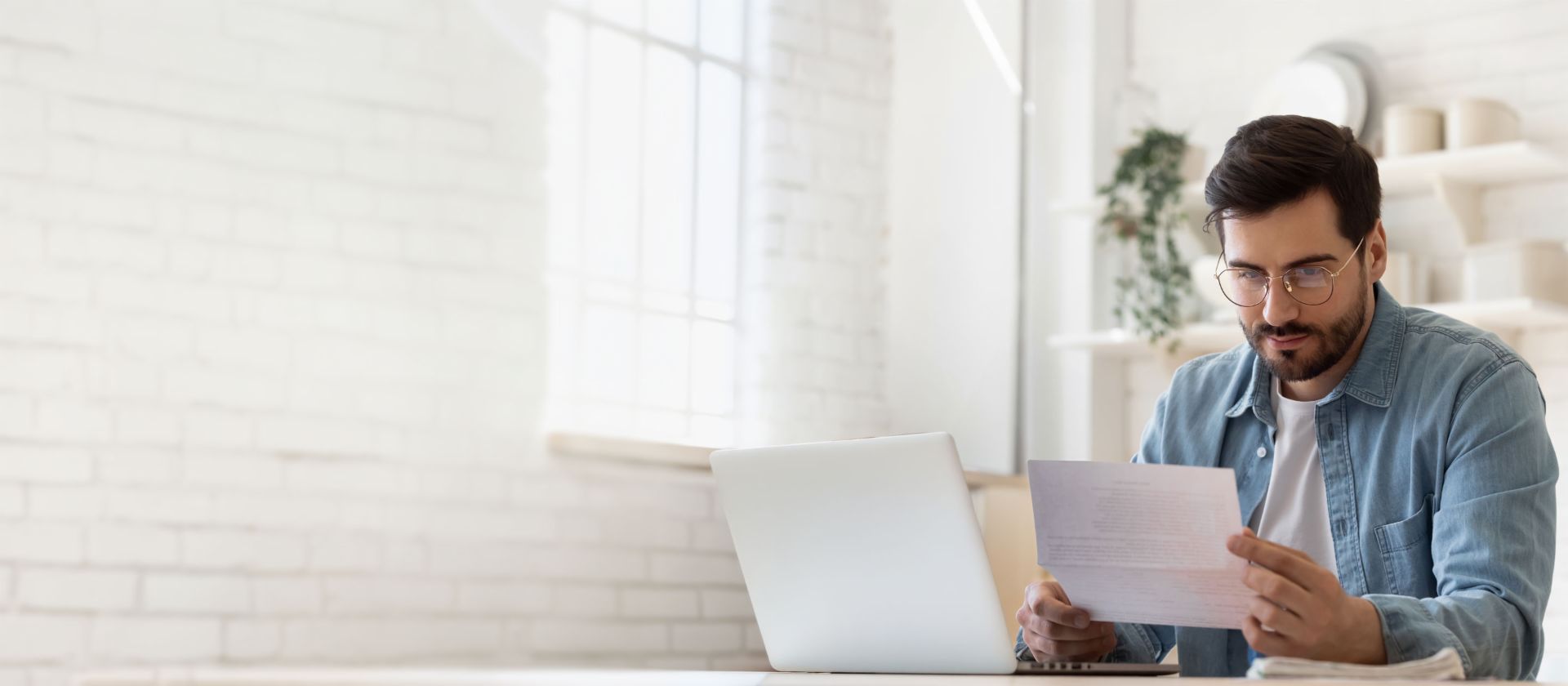 Man met bril werkt op laptop terwijl hij schuldregelingsdocument bekijkt in licht huis
