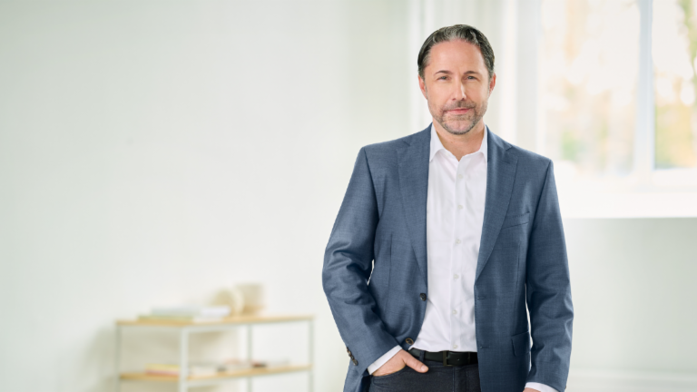 Marwin Ramcke, CEO, dans une pièce lumineuse, vêtu d’un costume bleu, la main droite dans la poche de son pantalon. 