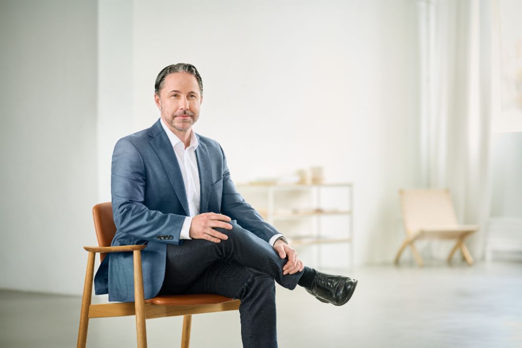 Portret van Marwin Ramcke, voorzitter van de Raad van Bestuur van de EOS-groep, die in een heldere ruimte zit en een donkere blazer draagt. 