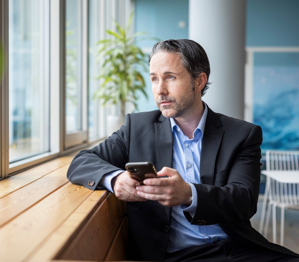 Marwin Ramcke zit op een bank en kijkt nadenkend uit het raam. Hij heeft een mobiele telefoon in zijn hand.