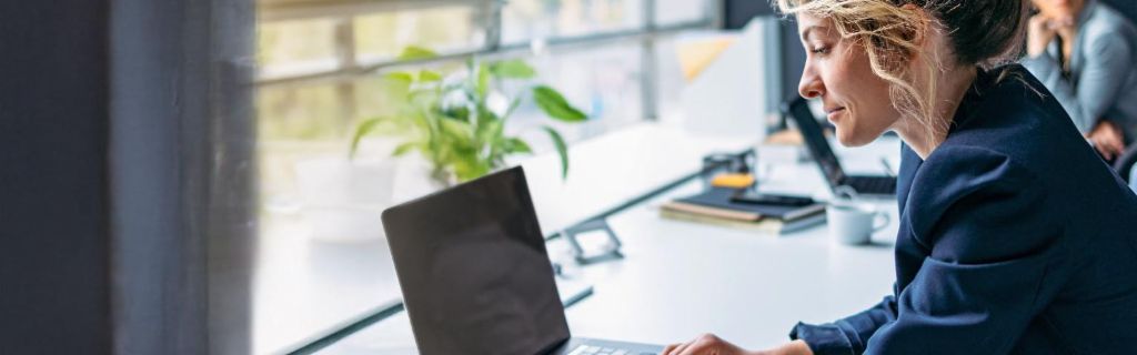 Jonge vrouw werkt op een laptop in een modern kantoor.