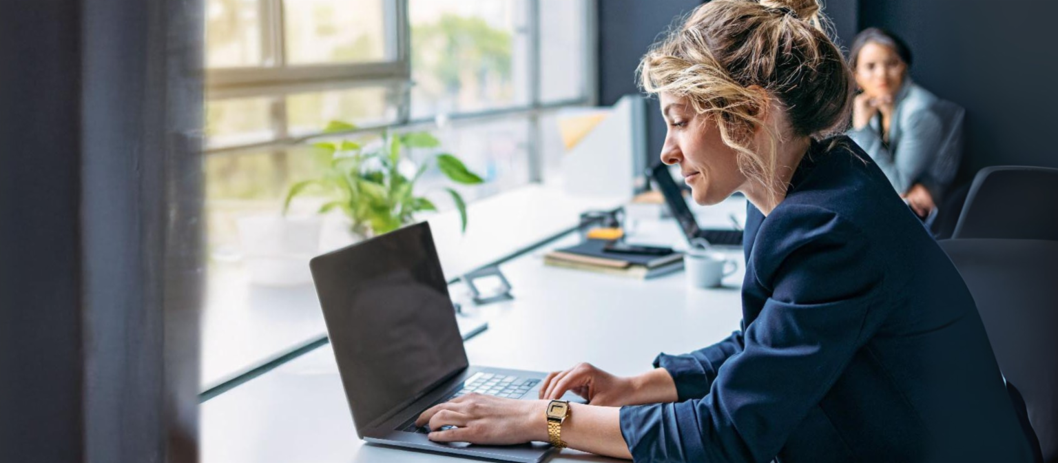 Jonge vrouw werkt op een laptop in een modern kantoor.