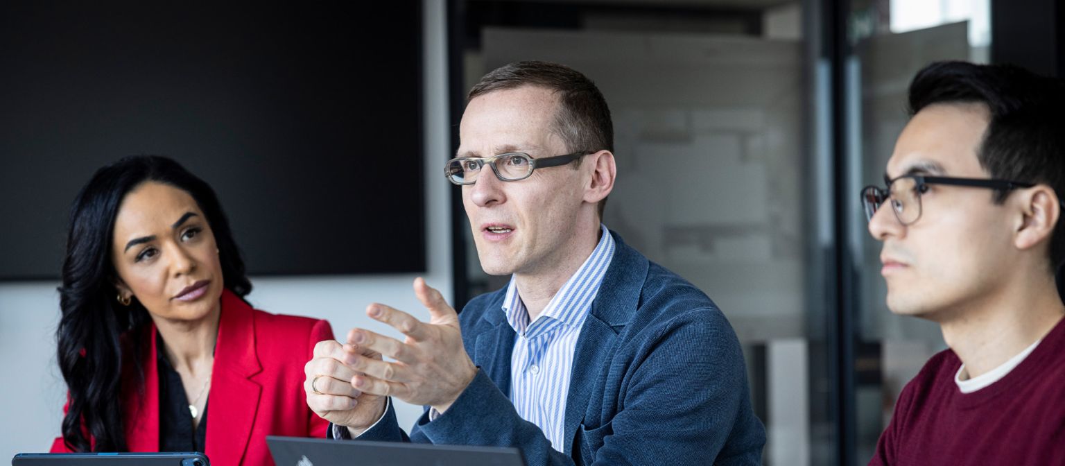 Drie mensen voeren een gesprek in een kantoor.