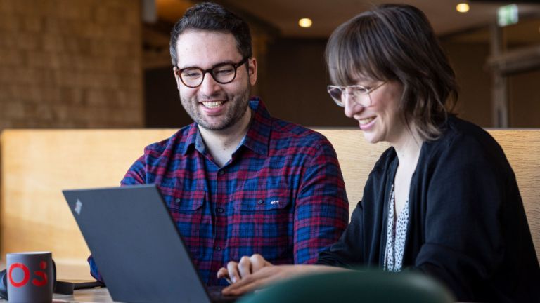 Twee EOS-medewerkers kijken samen naar een laptop terwijl ze verdiept zijn in een gesprek.