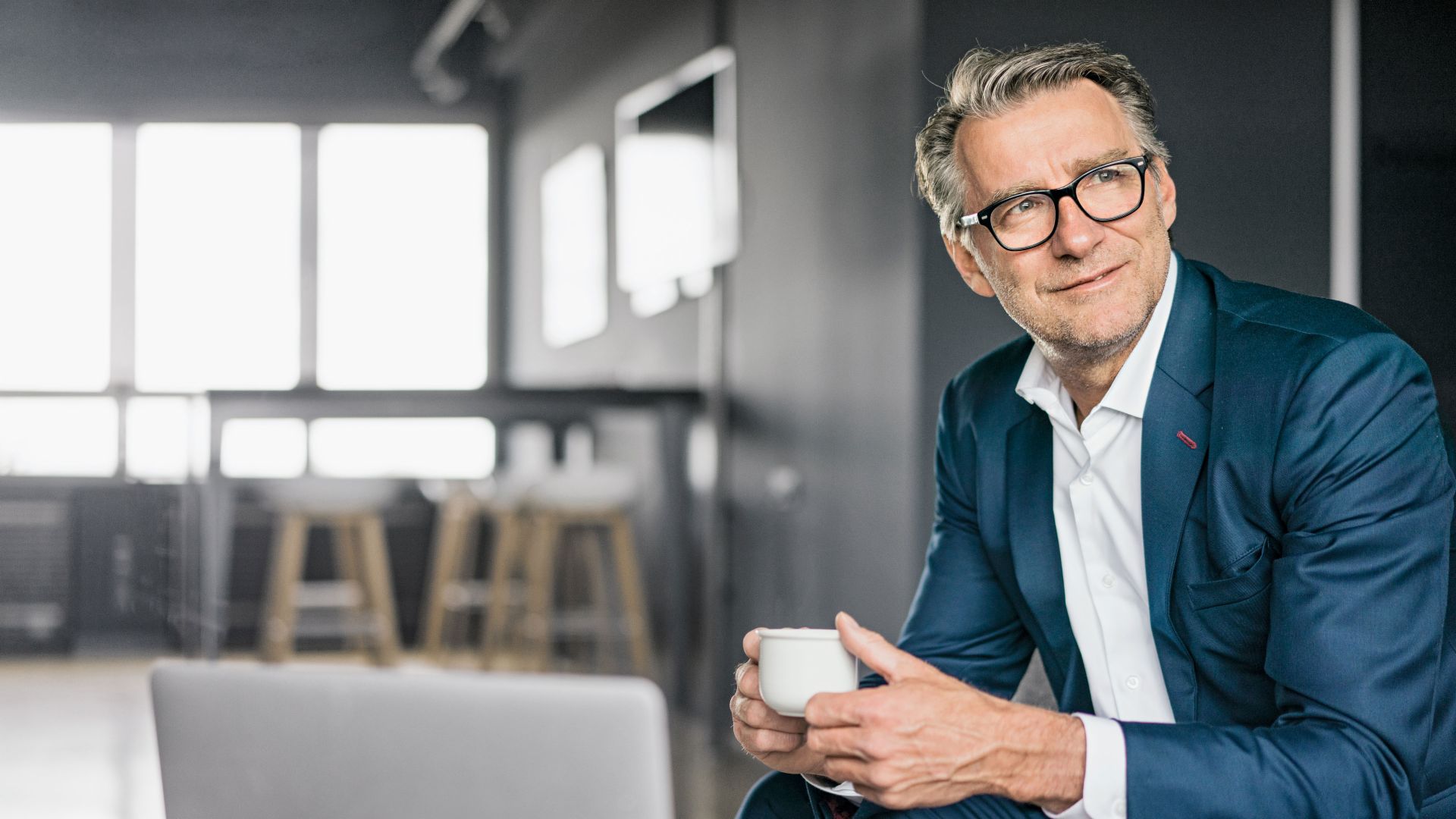 Portret van een zittende volwassen zakenman in een blauw pak die een witte koffiekop vasthoudt
