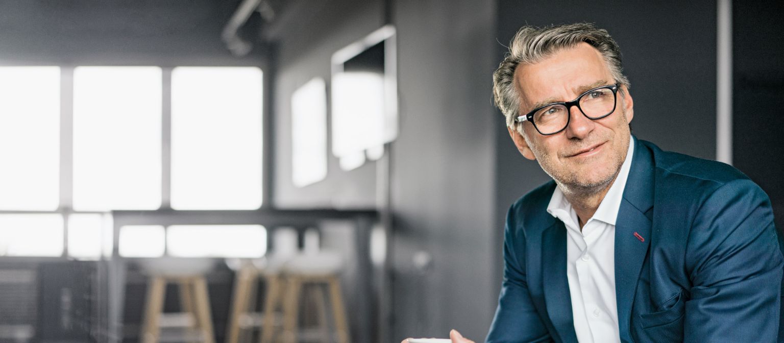 Portrait d'un homme d'affaires mûr assis, portant un costume bleu et tenant une tasse de café blanche