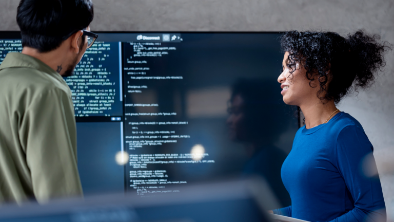 IA dans le recouvrement de créances : sur cette image, deux professionnels analysent collaborativement du code de programme pour des processus automatisés sur un grand écran. La scène illustre l'application pratique de l'intelligence artificielle (IA) et de l'automatisation des processus robotiques (RPA) dans la gestion des créances – un exemple de transformation numérique dans la gestion des créances.