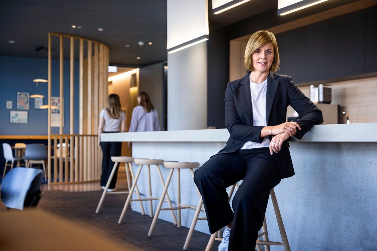 Dr. Eva Griewel, CFO van de EOS Groep, zit in een sociale ruimte op een hoge kruk, gekleed in een zwarte blazer.