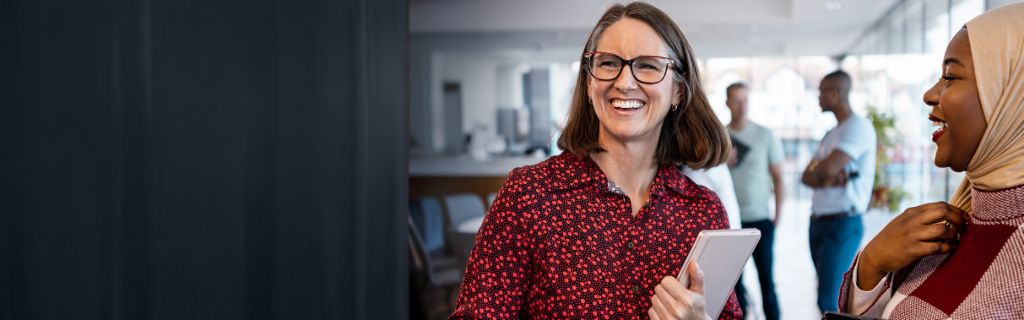 Twee vrolijke vrouwen die een informeel praatje maken op kantoor.