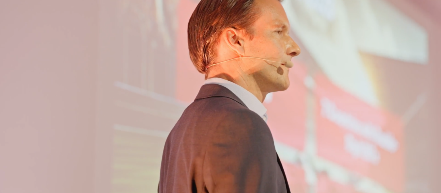 Profile shot of Carsten Tidow, Member of the EOS Group’s Board of Directors and responsible for Eastern Europe, on stage with a microphone and looking to the right. 