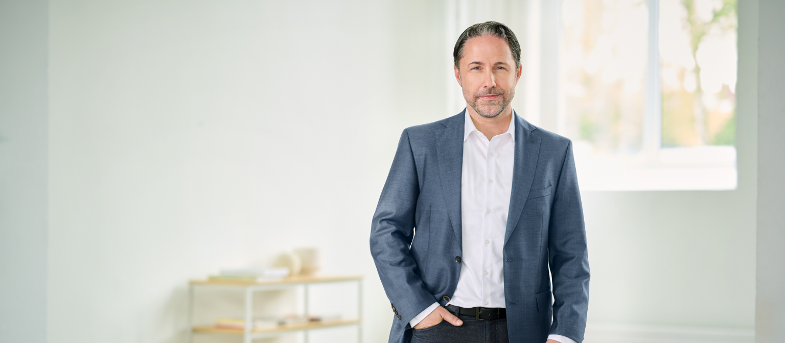 Marwin Ramcke, CEO, staat met een blauw pak en de rechterhand in zijn broekzak in een lichte ruimte. 