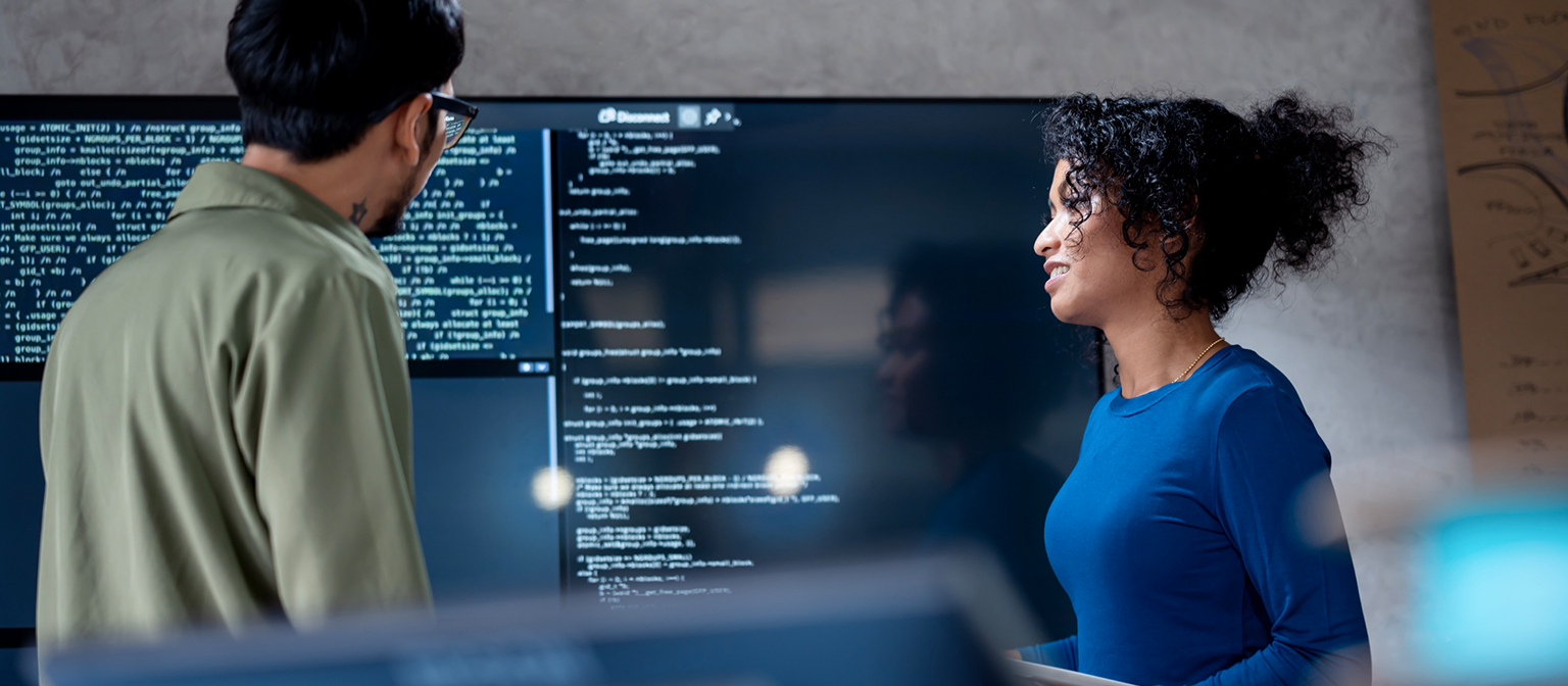 AI in incasso: In deze afbeelding analyseren twee professionals gezamenlijk programmacode voor geautomatiseerde processen op een groot scherm. De scène illustreert de praktische toepassing van Kunstmatige Intelligentie (AI) en Robotic Process Automation (RPA) in debiteurenbeheer – een voorbeeld van digitale transformatie in het beheer van vorderingen.