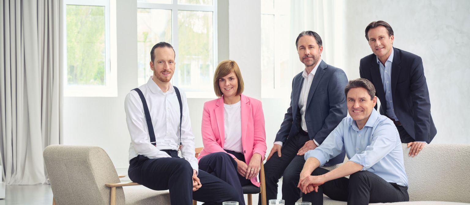 De Raad van Bestuur van de EOS-groep (van links naar rechts: Sebastian Pollmer, dr. Eva Griewel, Marwin Ramcke, dr. Stephan Ohlmeyer, Carsten Tidow) zit in een heldere ruimte en kijkt recht naar de camera.