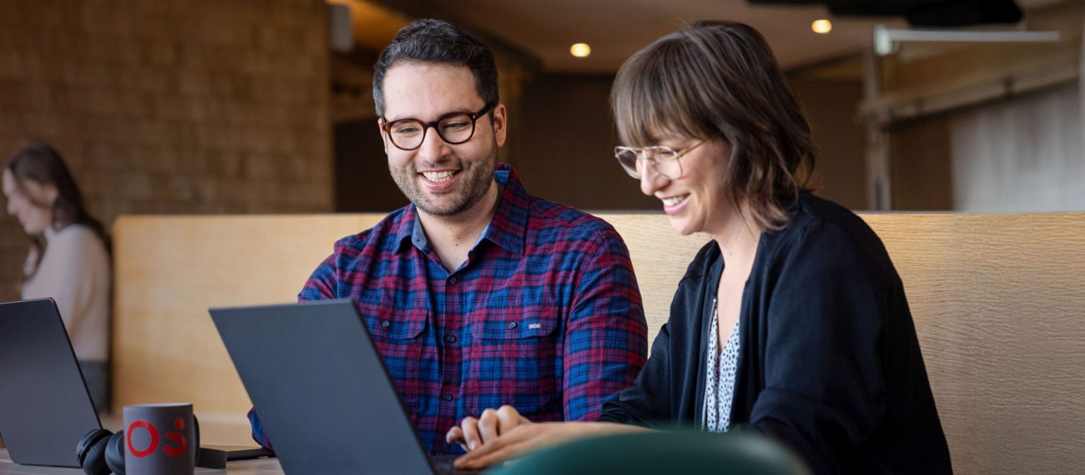 Twee EOS-medewerkers kijken samen naar een laptop terwijl ze verdiept zijn in een gesprek.
