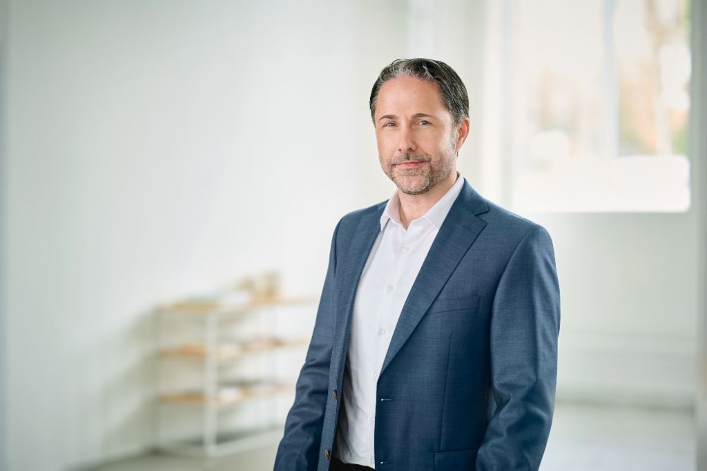 Portret van Marwin Ramcke, voorzitter van de Raad van Bestuur van de EOS-groep, die in een heldere ruimte zit en een donkere blazer draagt. 