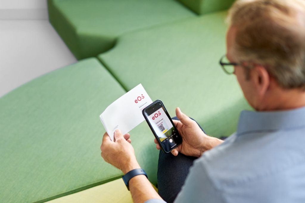 Een man scant een QR-code op een brief van EOS met zijn smartphone om zijn openstaande vordering online op het EOS Portaal te voldoen.